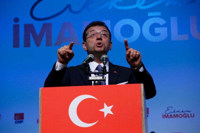 Ekrem Imamoglu fait des gestes alors qu'il prononce un discours sur un fond bleu